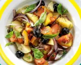 Insalata eoliana con patate, pomodori, olive nere, cipolla rossa e basilico fresco, servita in un piatto colorato.