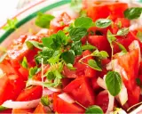 Un'insalata di pomodori freschi e succosi, condita con cipolla bianca e profumata erba aromatica.
