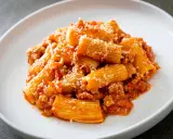 Un piatto di pasta alla zozzona, con rigatoni conditi con un ricco sugo di carne e pomodoro, spolverati di parmigiano.