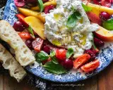 Insalata estiva con burrata, pesche, ciliegie, pomodorini e basilico, condita con olio e pinoli. Accompagnata da pane casereccio.