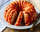 Un invitante timballo di pasta, con spaghetti avvolti in un ricco sugo rosso, servito su un piatto bianco con un coltello dorato.