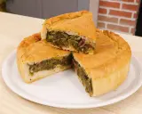 Una fetta di pizza di scarola, ricca di verdure e olive, su un piatto bianco.