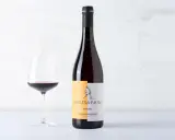 Calice di vino rosso accanto a una bottiglia di Grignolino d'Asti Carlin de Paolo. Un vino che ricorda il barbera vitigno per la sua vivacità.