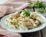 Piatto di pasta panna e salmone, guarnito con prezzemolo fresco, servito su un piatto bianco.