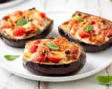 Melanzane ripiene vegetariane, gustose e colorate, con pomodorini e formaggio filante, guarnite con basilico fresco.