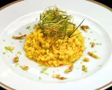 Risotto giallo intenso con fiori di zucca e zafferano, guarnito con erbe croccanti.