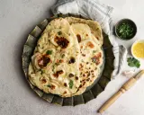 Pane in padella soffice e dorato, guarnito con erbe fresche. Accanto, ciotoline con olio e coriandolo, uno spicchio d'aglio e un pennello da cucina.