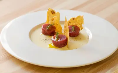 Tre cilindri di tartare di manzo, guarniti con timo, su una crema chiara e croccanti cialde. Un'idea su come condirla.