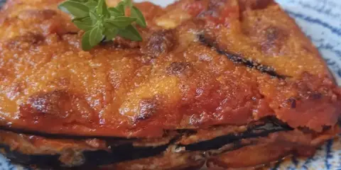 Parmigiana in padella, uno strato di melanzane fritte, pomodoro e formaggio, guarnita con basilico fresco.