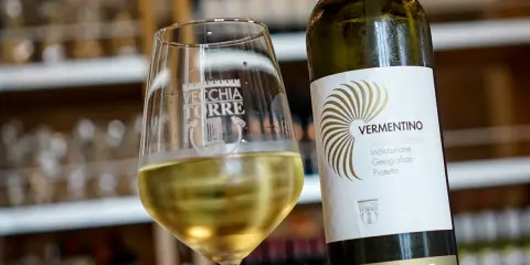 Un bicchiere di vino bianco Vermentino, frizzante e dorato, accanto alla sua bottiglia Vecchia Torre.