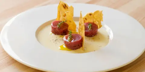 Tre cilindri di tartare di manzo, guarniti con timo, su una crema chiara e croccanti cialde. Un'idea su come condirla.