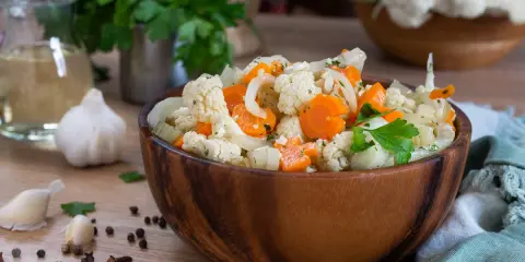 Un'appetitosa giardiniera in agrodolce, con cavolfiore, carote e cipolle, servita in una ciotola di legno.
