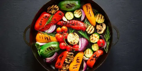 Un assortimento colorato di verdure grigliate, tra cui peperoni, zucchine, cipolle rosse e pomodorini, disposte in una padella di ghisa.