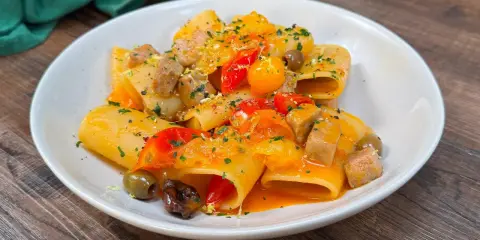 Paccheri con tonno fresco, pomodorini, olive e scorza di limone. Un piatto colorato e saporito, pronto per essere gustato.