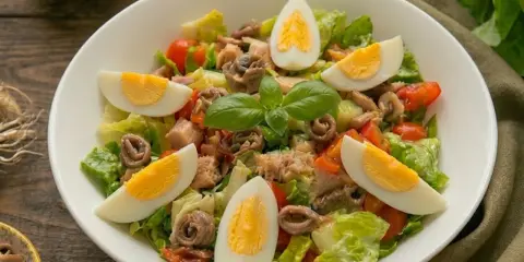 Insalata nizzarda con uova sode, tonno, acciughe, pomodorini e lattuga. Ingredienti freschi per un piatto gustoso.