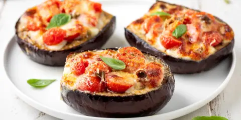 Melanzane ripiene vegetariane, gustose e colorate, con pomodorini e formaggio filante, guarnite con basilico fresco.