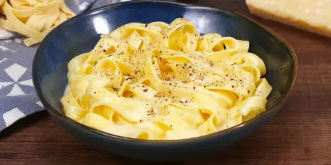 Un piatto di fettuccine alfredo fumanti, condite con una cremosa salsa al parmigiano e pepe nero.