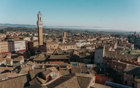Vista aerea di Siena, con la Torre del Mangia in primo piano. Un'idea per cosa vedere in Toscana in 2 giorni, tra tetti in cotto e colline nebbiose.