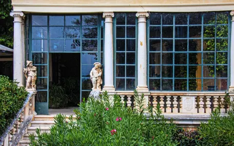 Statue di nani custodi di un giardino lussureggiante sui Colli Berici, con un'elegante serra sullo sfondo.