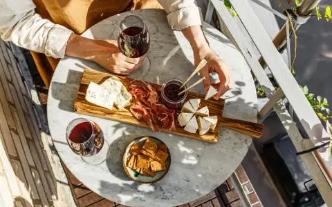Un tagliere con formaggi, salumi e marmellata, accompagnato da un bicchiere di vino rosso. Le caratteristiche del nebbiolo vino si esaltano con questi sapori.