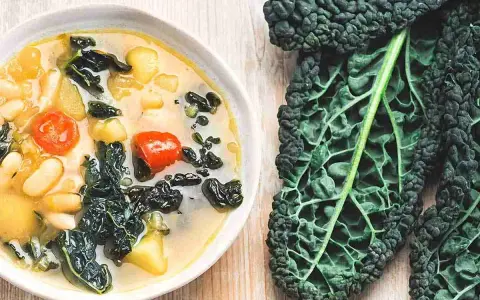 Zuppa ricca con fagioli, pomodoro e il sapore intenso del cavolo nero. Accanto, una foglia di cavolo nero fresca.