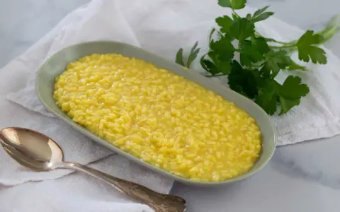 Un cremoso risotto al pistacchio, servito in un piatto ovale con un cucchiaio d'argento e un rametto di prezzemolo fresco.