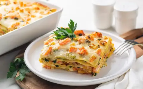Una fetta di lasagne di pesce, stratificata con salmone e zucchine, guarnita con prezzemolo.