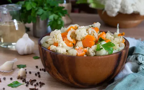 Un'appetitosa giardiniera in agrodolce, con cavolfiore, carote e cipolle, servita in una ciotola di legno.
