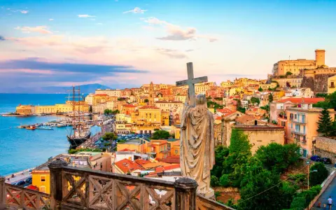 Statua con croce domina la vista di Gaeta, perfetta per una gita fuori porta da Roma. Porto, case colorate e castello sullo sfondo.
