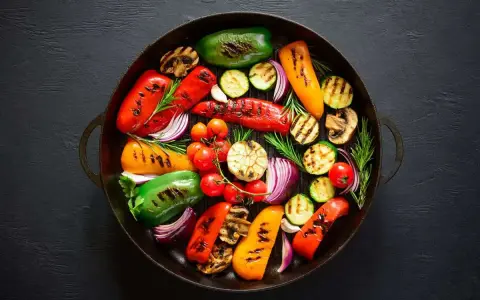 Un assortimento colorato di verdure grigliate, tra cui peperoni, zucchine, cipolle rosse e pomodorini, disposte in una padella di ghisa.