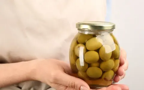 Mani che tengono un barattolo di olive verdi in salamoia per olive, pronte per essere gustate.