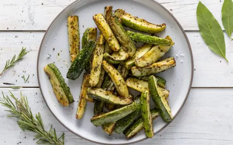 Zucchine in friggitrice ad aria, tagliate a bastoncini e condite con erbe aromatiche, pronte per essere gustate.