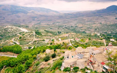 Panoramica di Contessa Entellina, un borgo siciliano tra colline verdi e campi coltivati, con case dai tetti in cotto e una strada tortuosa.