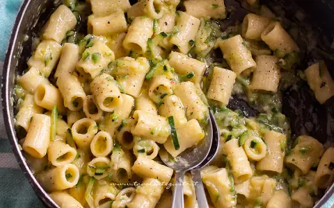 Primo piatto di pasta con pancetta e zucchine, condito con una crema saporita e pepe nero.