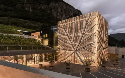 Cantina Sociale Bolzano: edificio moderno con facciata luminosa a forma di foglia, circondato da vigneti e montagne.