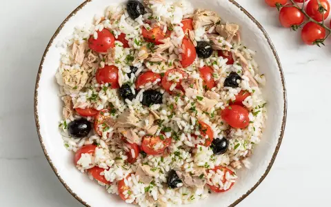 Insalata di riso con tonno, pomodorini, olive nere e prezzemolo. Un'idea fresca e gustosa su come condire l'insalata di riso per un pranzo estivo.