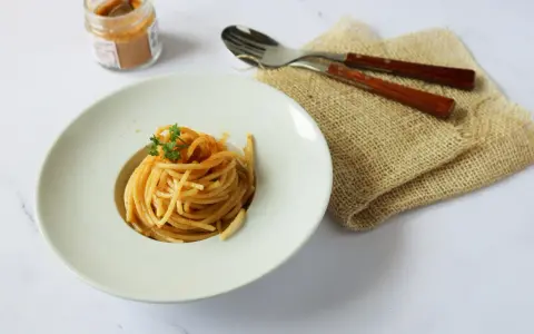 Spaghetti alla bottarga, un piatto semplice ma gustoso, pronto per essere assaporato. Un vasetto di bottarga in polvere e posate completano la scena.