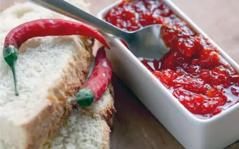 Fette di pane con peperoncini rossi e una ciotolina di marmellata di peperoncino, pronta per essere gustata.