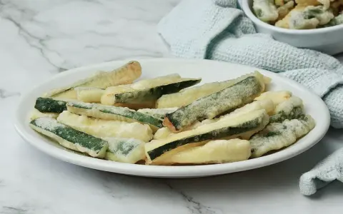 Zucchine fritte in pastella dorata, croccanti e invitanti, servite su un piatto bianco.