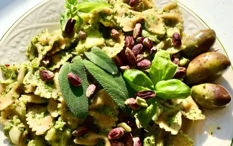 Farfalle condite con un saporito pesto di salvia, guarnite con pistacchi, basilico e olive verdi.