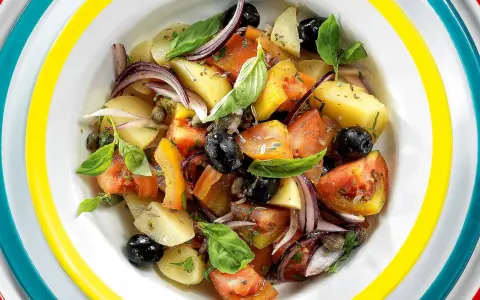 Insalata eoliana con patate, pomodori, olive nere, cipolla rossa e basilico fresco, servita in un piatto colorato.