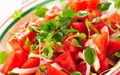 Un'insalata di pomodori freschi e succosi, condita con cipolla bianca e profumata erba aromatica.