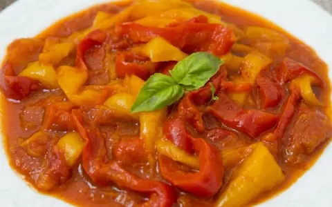 Peperonata ricetta della nonna: peperoni rossi e gialli cotti lentamente in un sugo saporito, guarniti con basilico fresco.