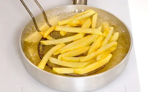 Patate fritte dorate che sfrigolano nell'olio bollente, pronte per essere gustate.