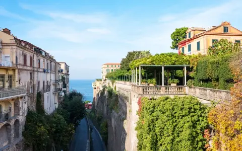 Edifici affacciati sul mare blu, con un viale alberato che scende verso la costa. La **penisola sorrentina** offre scorci mozzafiato tra ville storiche e vegetazione rigogliosa.