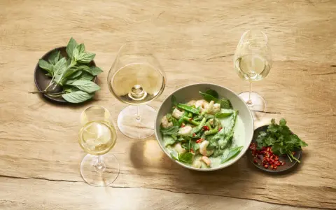 Un curry verde con gamberi e verdure, accompagnato da bicchieri di vino bianco, evoca le fresche **sauvignon blanc caratteristiche**.