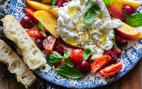 Insalata estiva con burrata, pesche, ciliegie, pomodorini e basilico, condita con olio e pinoli. Accompagnata da pane casereccio.