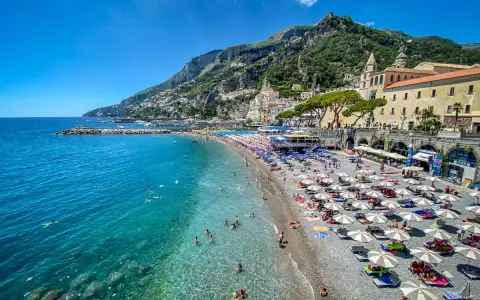 Spiaggia affollata con ombrelloni e gente che nuota in acque cristalline. Un'idea perfetta per decidere dove andare un weekend in Italia.