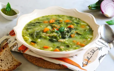 Un fumante minestrone genovese, ricco di verdure fresche, piselli, carote e fagioli, servito con pesto e pane tostato.