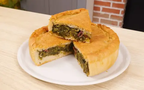Una fetta di pizza di scarola, ricca di verdure e olive, su un piatto bianco.